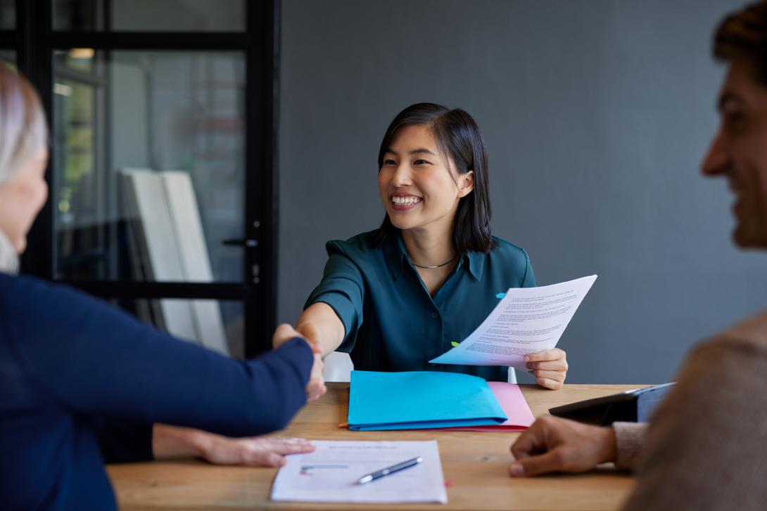 a professional woman shakes hands with a woman across a desk